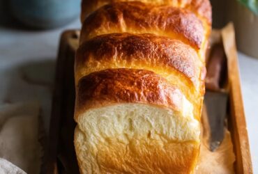 Loaf of light and fluffy Japanese milk bread with golden top and pull-apart sections on a wooden board