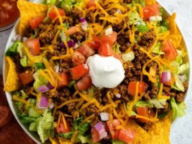 Doritos taco salad in a wooden bowl with seasoned ground beef, melted cheddar, lettuce, tomato, sour cream, and crushed Doritos on top