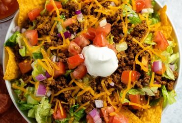 Doritos taco salad in a wooden bowl with seasoned ground beef, melted cheddar, lettuce, tomato, sour cream, and crushed Doritos on top