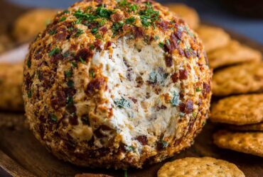 Cowboy cream cheese ball coated in crispy bacon, shredded cheddar, and chopped scallions on a wooden board with crackers