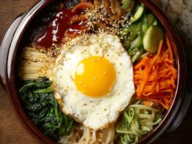 Bibimbap Korean rice bowl in a stone dol sot with marinated beef bulgogi, sautéed spinach, carrots, mushrooms, bean sprouts, fried egg, and gochujang sauce