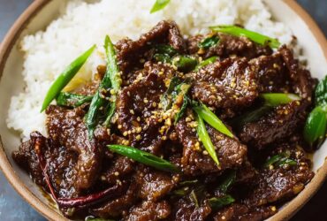 Mongolian beef with crispy edges, glossy sweet-soy sauce, sliced scallions, and steamed white rice on a black plate