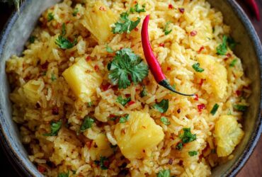 Pineapple rice served in a hollowed pineapple half with cashews, scallions, and golden curry-tinted jasmine rice