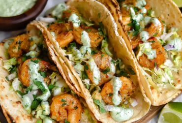 Shrimp tacos with golden seared shrimp, shredded cabbage, avocado, and spicy cilantro lime sauce drizzled on top
