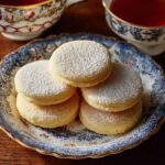 Stack of old-fashioned Southern tea cakes with golden edges, soft centers, light vanilla glaze, and powdered sugar dusting