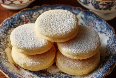 Stack of old-fashioned Southern tea cakes with golden edges, soft centers, light vanilla glaze, and powdered sugar dusting