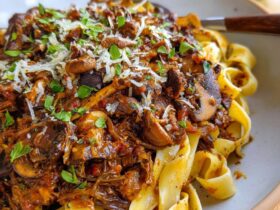 Mushroom ragu over wide pappardelle pasta with deep red wine sauce, fresh thyme, parmesan shavings, and cracked pepper