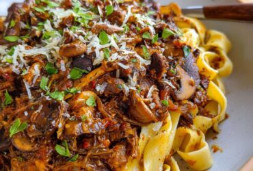 Mushroom ragu over wide pappardelle pasta with deep red wine sauce, fresh thyme, parmesan shavings, and cracked pepper