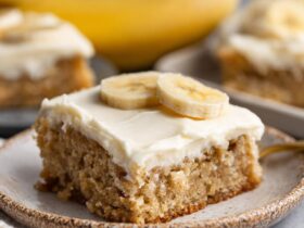 Banana bars cut into squares with thick fluffy cream cheese frosting, golden moist banana cake, and chopped walnuts on top