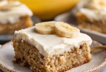 Banana bars cut into squares with thick fluffy cream cheese frosting, golden moist banana cake, and chopped walnuts on top