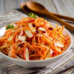 Carrot apple salad in a wooden bowl with shredded carrots, julienned apple, golden raisins, walnuts, fresh dill, and creamy citrus dressing