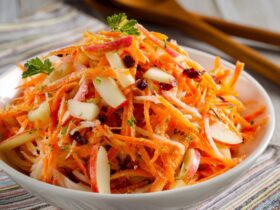 Carrot apple salad in a wooden bowl with shredded carrots, julienned apple, golden raisins, walnuts, fresh dill, and creamy citrus dressing