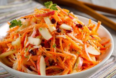 Carrot apple salad in a wooden bowl with shredded carrots, julienned apple, golden raisins, walnuts, fresh dill, and creamy citrus dressing