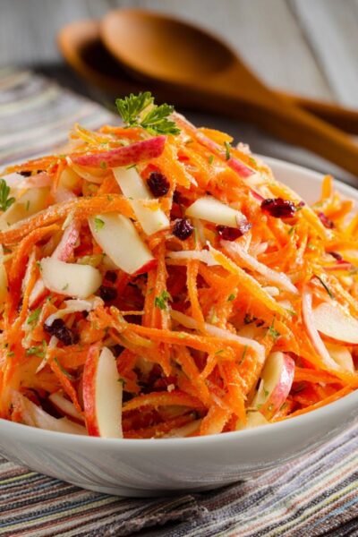 Carrot apple salad in a wooden bowl with shredded carrots, julienned apple, golden raisins, walnuts, fresh dill, and creamy citrus dressing