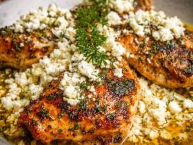 Greek chicken with lemon, feta, oregano, and olives in a sheet pan with golden crispy skin and bright Mediterranean colors