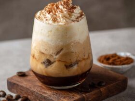 Tiramisu cold brew in a tall glass with layers of mascarpone cream, espresso cold brew, cocoa dust, and ladyfinger garnish
