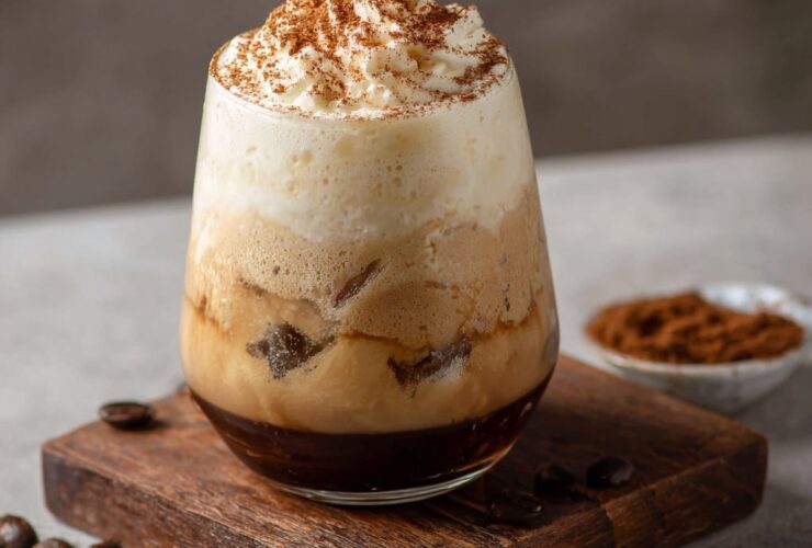 Tiramisu cold brew in a tall glass with layers of mascarpone cream, espresso cold brew, cocoa dust, and ladyfinger garnish