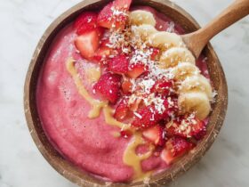 Strawberry banana smoothie bowl with thick pink purée, fresh strawberries, banana slices, granola, chia seeds, and coconut flakes on top