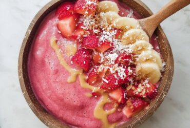 Strawberry banana smoothie bowl with thick pink purée, fresh strawberries, banana slices, granola, chia seeds, and coconut flakes on top