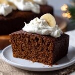 Gingerbread cake with white powdered sugar dusting, candied orange peel, fresh rosemary, and visible spice flecks in dark brown crumb