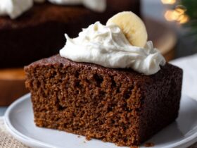 Gingerbread cake with white powdered sugar dusting, candied orange peel, fresh rosemary, and visible spice flecks in dark brown crumb