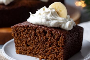 Gingerbread cake with white powdered sugar dusting, candied orange peel, fresh rosemary, and visible spice flecks in dark brown crumb