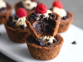 Bite-sized brownie tarts with fudgy chocolate cups, glossy chocolate ganache filling, fresh raspberry, and gold leaf garnish