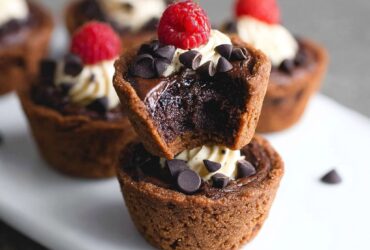 Bite-sized brownie tarts with fudgy chocolate cups, glossy chocolate ganache filling, fresh raspberry, and gold leaf garnish