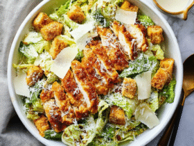 Crispy panko-breaded chicken strips on crisp romaine Caesar salad with parmesan shavings, croutons, and creamy Caesar dressing in a wooden bowl