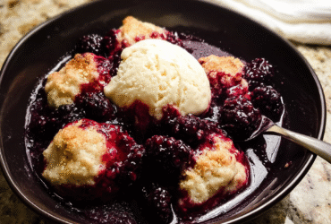 Triple berry cobbler in a dark plate with bubbling blackberry-blueberry-raspberry filling, golden biscuit topping, vanilla ice cream melting on top