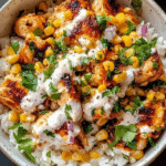 Street corn chicken rice bowl with seasoned chicken cubes, charred corn, white cotija crema, cilantro, red onion, lime over white rice