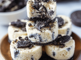 Oreo cheesecake bites on a white plate with crushed Oreo crust, creamy cheesecake filling, Oreo chunks, white chocolate drizzle, mini cookies