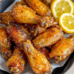 Honey lemon pepper wings in a black bowl with crispy golden glazed wings, lemon slices, fresh black pepper, garnished with chopped parsley