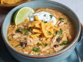 White chicken chili in a rustic bowl with shredded chicken, white beans, green chiles, creamy broth, topped with cheese, cilantro, lime, tortilla strips