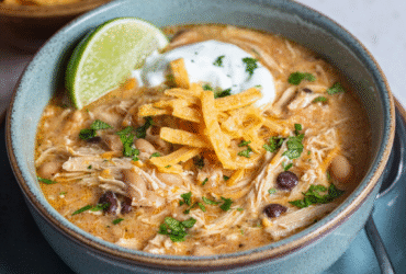 White chicken chili in a rustic bowl with shredded chicken, white beans, green chiles, creamy broth, topped with cheese, cilantro, lime, tortilla strips