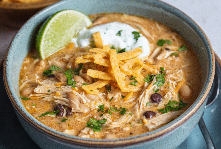 White chicken chili in a rustic bowl with shredded chicken, white beans, green chiles, creamy broth, topped with cheese, cilantro, lime, tortilla strips