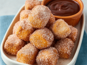 Sweet air fryer churro bites coated in cinnamon sugar on a white plate with chocolate dipping sauce, golden crispy outside and pillowy inside