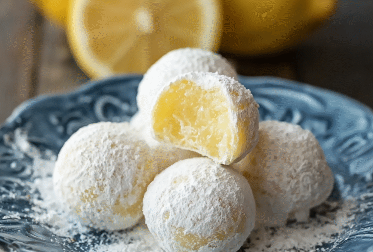 Lemon truffles on a marble surface dusted with powdered sugar, pale yellow centers visible, lemon zest scattered around, fresh lemon halves