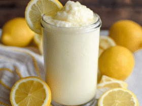 Chick-fil-A frosted lemonade copycat in a tall glass with thick creamy texture, lemon slice on the rim, pale yellow color, whipped cream on top