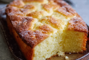 French butter cake on a serving plate with golden crosshatched top, deep amber color, dusting of powdered sugar, slice cut showing dense texture