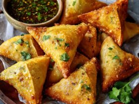 Crispy golden samosas with dipping sauce on a plate, showing flaky pastry triangles filled with spiced potato and peas, served with mint chutney and tamarind sauce