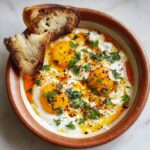 Shakshuka in a cast-iron skillet with poached eggs nestled in chunky tomato sauce, red bell peppers, feta crumbles, fresh parsley, served with toasted bread