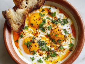 Shakshuka in a cast-iron skillet with poached eggs nestled in chunky tomato sauce, red bell peppers, feta crumbles, fresh parsley, served with toasted bread