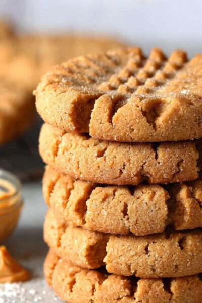Peanut butter cookies on a wooden board with classic crosshatch fork pattern on top, golden edges, soft chewy centers, sea salt sprinkle