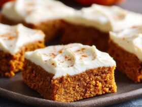 Pumpkin bars with cream cheese frosting cut into squares on a wooden board, moist orange pumpkin cake with thick white frosting, cinnamon dust on top