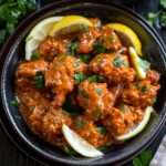Butter chicken in a serving bowl with tender chicken pieces in rich orange-red creamy tomato sauce, swirl of cream, fresh cilantro garnish, served with basmati rice
