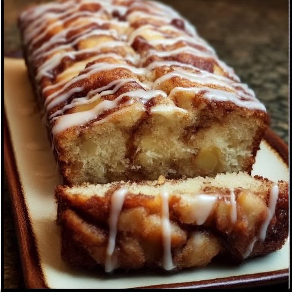 Cinnamon roll bread with icing on a wooden board, sliced loaf revealing soft cinnamon-sugar swirl, generous white vanilla icing drizzled across the top