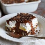 Chocolate lasagna dessert squares on a plate showing distinct layers of Oreo crust, cream cheese, chocolate pudding, whipped Cool Whip topping, chocolate shavings