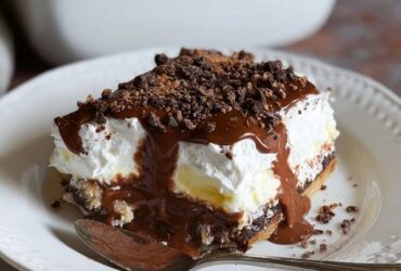 Chocolate lasagna dessert squares on a plate showing distinct layers of Oreo crust, cream cheese, chocolate pudding, whipped Cool Whip topping, chocolate shavings