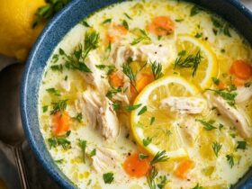 Lemon chicken soup in a white bowl with shredded chicken, orzo pasta, silky lemon-egg broth, lemon slices, fresh dill garnish, golden surface from emulsified egg
